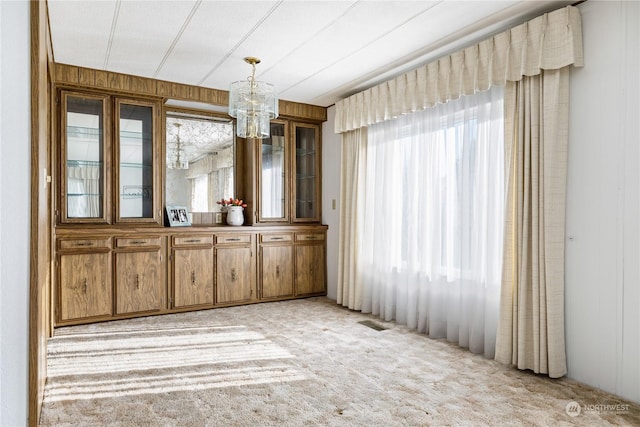 unfurnished dining area with an inviting chandelier, light colored carpet, and wood walls