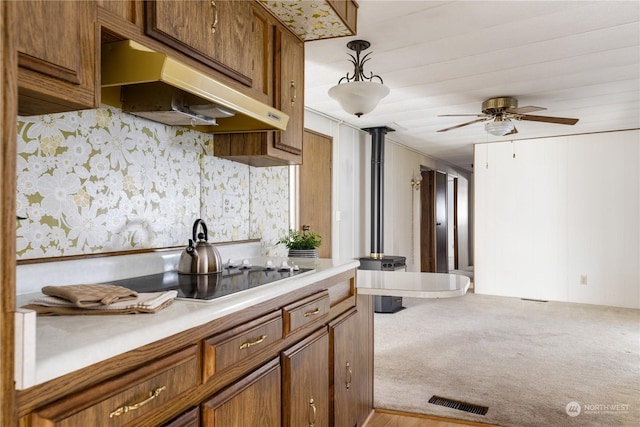 kitchen with black electric stovetop, light colored carpet, ceiling fan, and decorative light fixtures