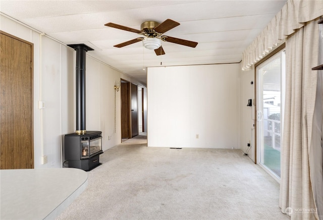 unfurnished living room with a wood stove, light colored carpet, and ceiling fan