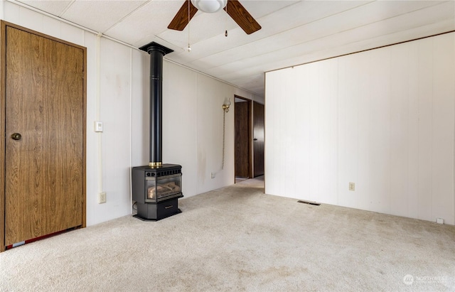 unfurnished living room featuring carpet floors, ceiling fan, and a wood stove