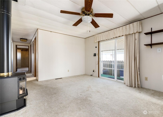 unfurnished living room with a wood stove, light carpet, and ceiling fan