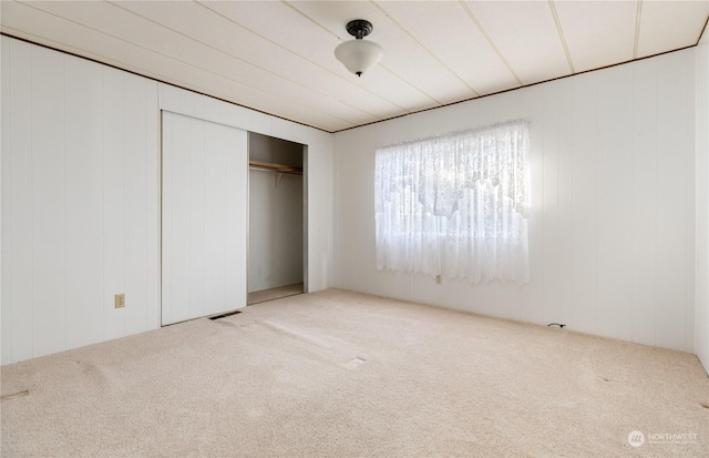 unfurnished bedroom with carpet, a closet, and wood walls