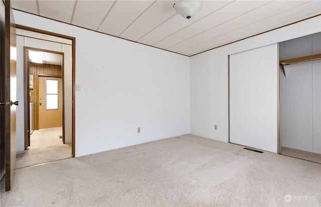 unfurnished bedroom featuring light carpet, wooden walls, and a closet