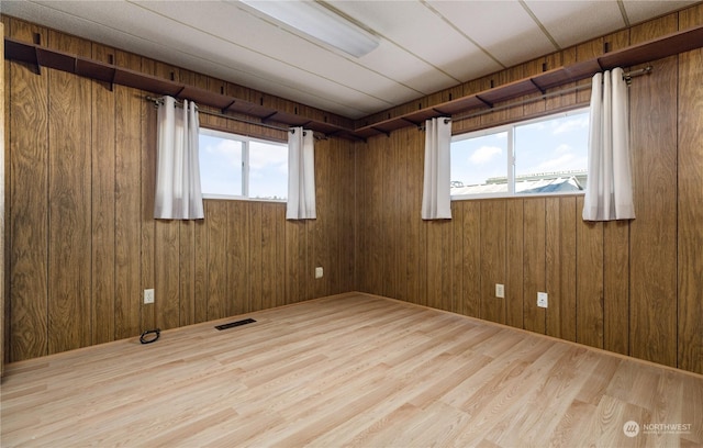 unfurnished room with wood-type flooring, wooden walls, and a healthy amount of sunlight