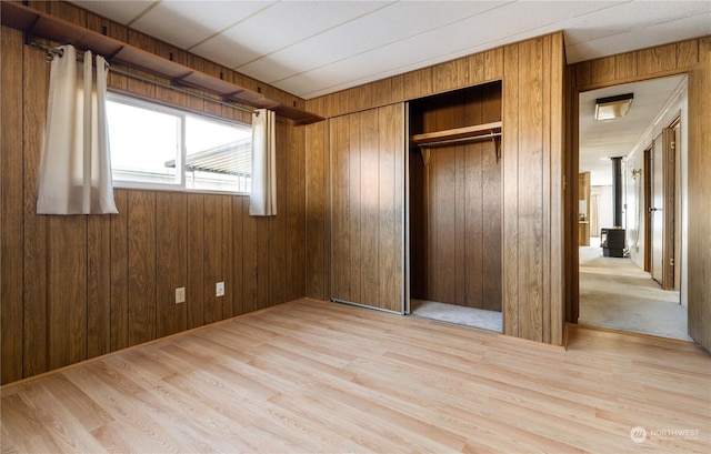 unfurnished bedroom with light hardwood / wood-style floors, a closet, and wood walls