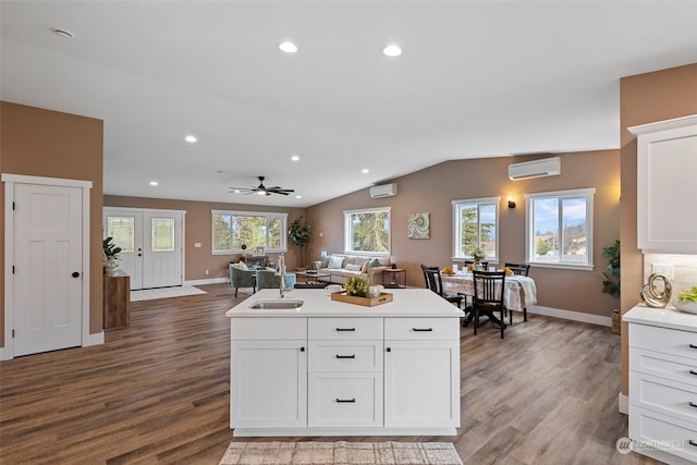 kitchen with vaulted ceiling, an AC wall unit, white cabinetry, wood-type flooring, and sink