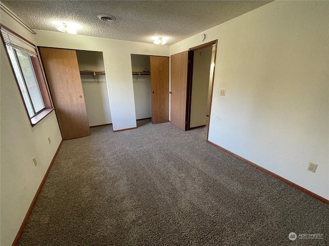 unfurnished bedroom featuring light carpet, multiple closets, and a textured ceiling