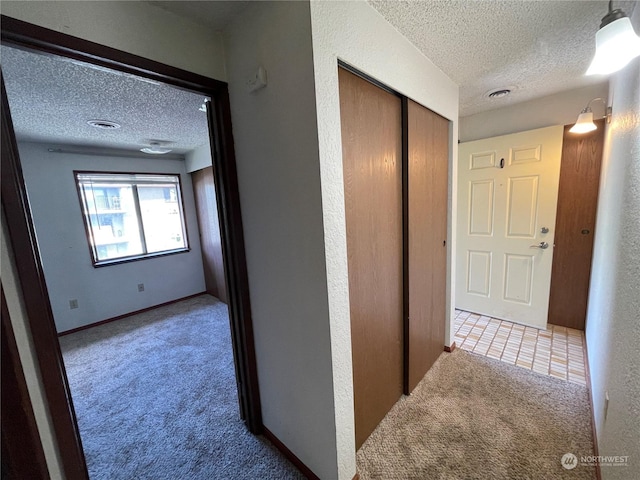 corridor with light carpet and a textured ceiling