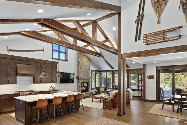 kitchen with pendant lighting, premium range hood, a kitchen island with sink, a kitchen breakfast bar, and a healthy amount of sunlight