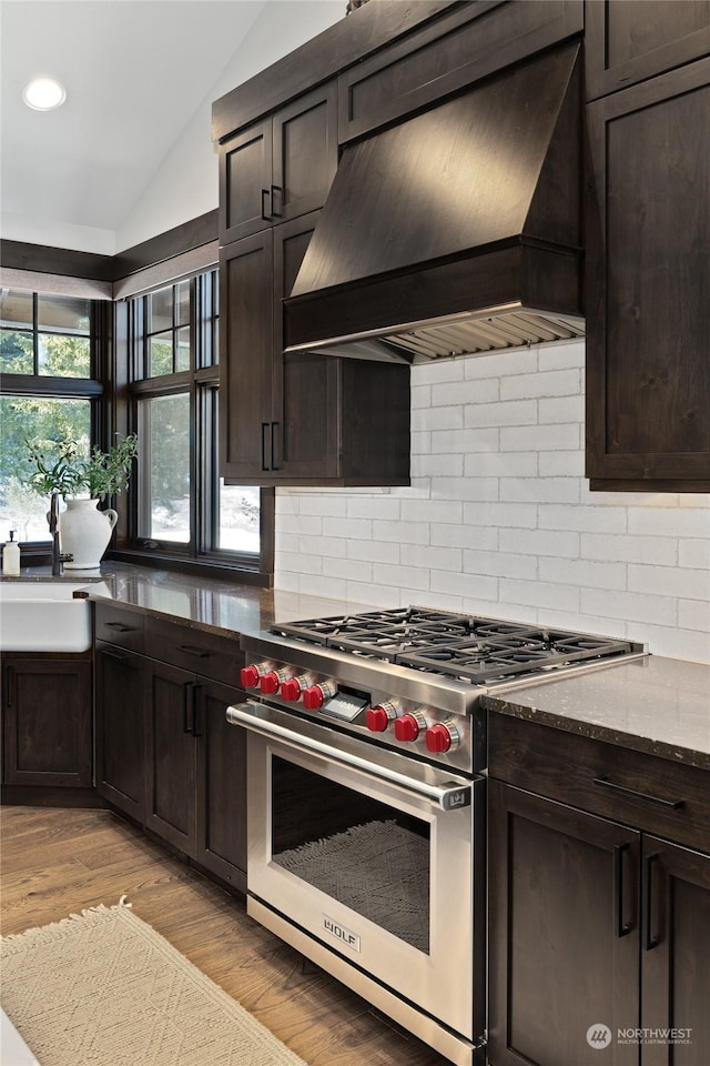 kitchen featuring stone counters, premium range hood, vaulted ceiling, premium stove, and light hardwood / wood-style floors