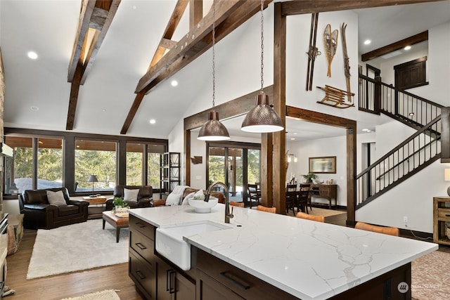 kitchen with pendant lighting, beamed ceiling, an island with sink, sink, and light stone counters