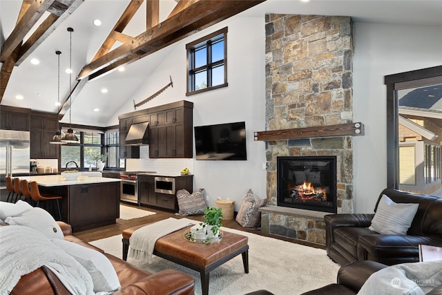 living room featuring high vaulted ceiling, a fireplace, sink, beam ceiling, and light wood-type flooring