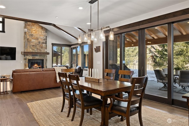 dining area featuring wood-type flooring, a stone fireplace, and high vaulted ceiling