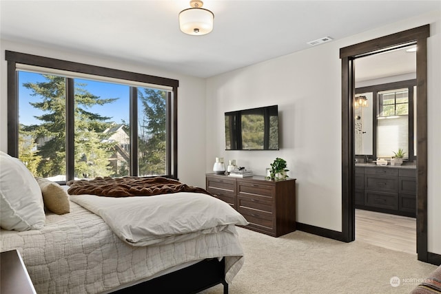 bedroom featuring connected bathroom and light carpet