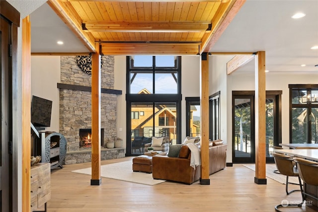 living room featuring beamed ceiling, a stone fireplace, wood ceiling, and light hardwood / wood-style flooring