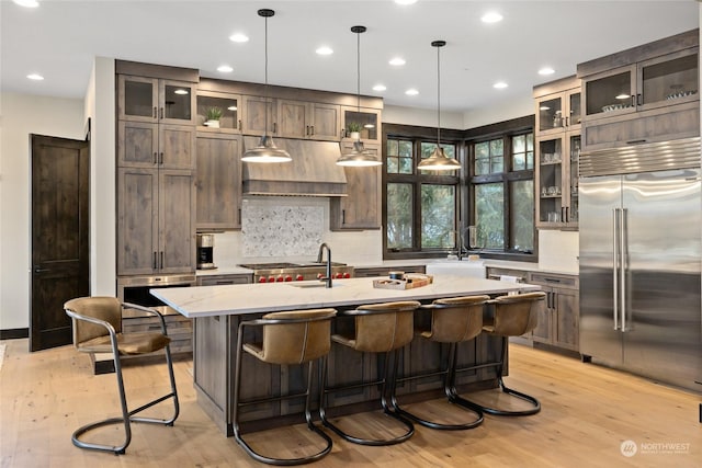 kitchen featuring decorative light fixtures, a kitchen island with sink, stainless steel appliances, light stone countertops, and light hardwood / wood-style floors