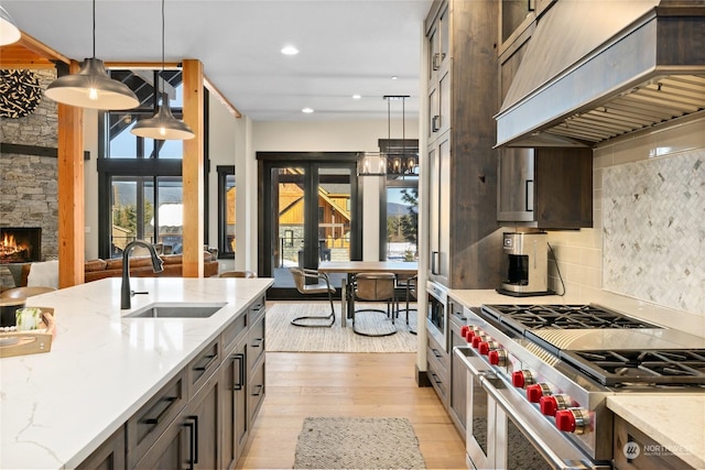 kitchen featuring pendant lighting, sink, light stone counters, custom range hood, and range with two ovens