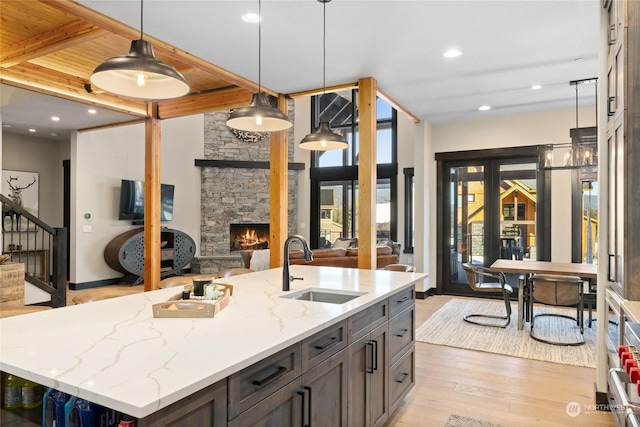 kitchen with sink, light hardwood / wood-style flooring, hanging light fixtures, light stone counters, and a center island with sink