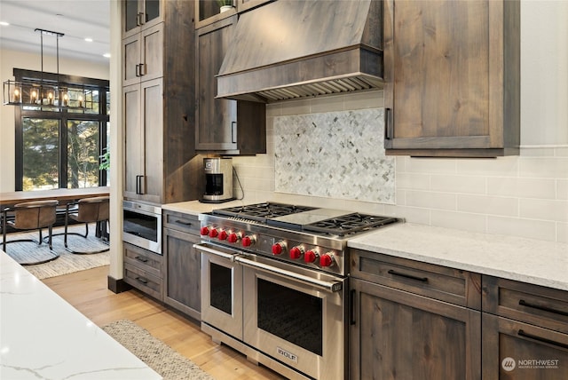 kitchen with custom exhaust hood, light stone countertops, light hardwood / wood-style floors, and range with two ovens