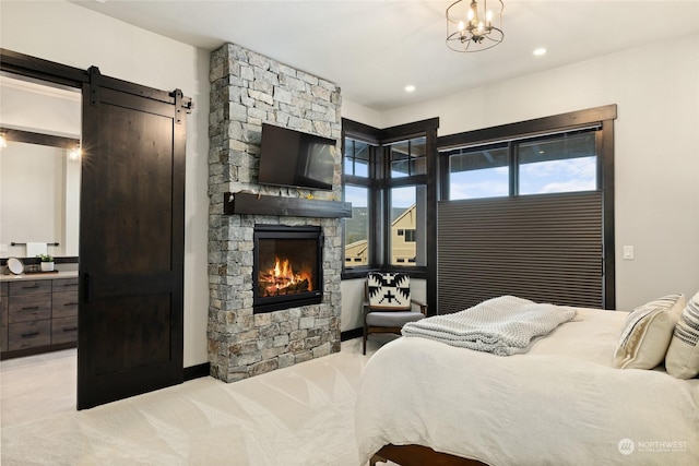 carpeted bedroom featuring an inviting chandelier, a barn door, and a stone fireplace