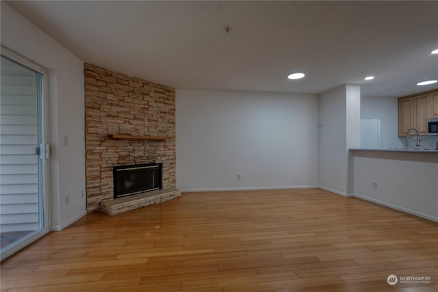 unfurnished living room with a fireplace, sink, and light hardwood / wood-style flooring