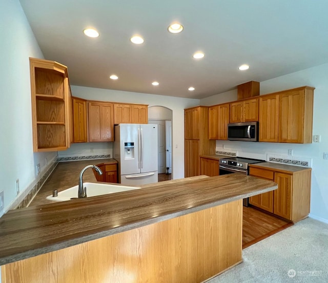 kitchen with a sink, a peninsula, arched walkways, stainless steel appliances, and open shelves