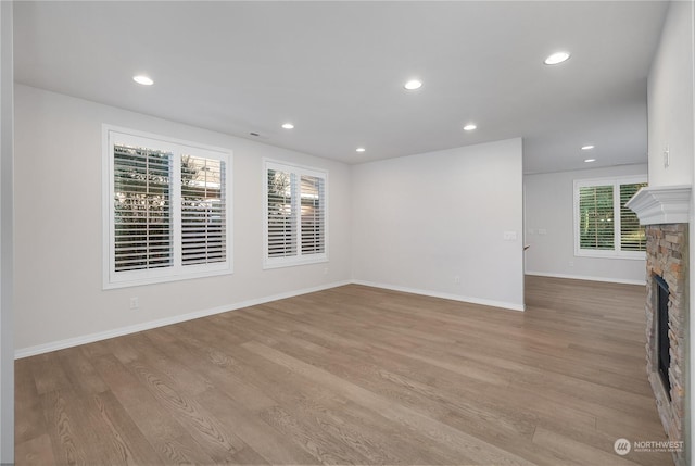 unfurnished living room with a stone fireplace and light hardwood / wood-style floors