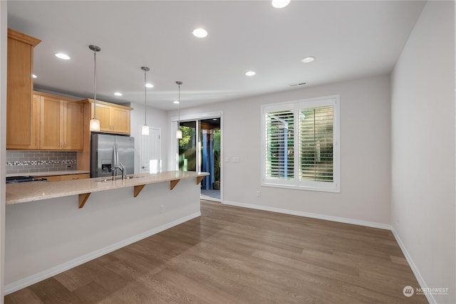 kitchen with stainless steel refrigerator with ice dispenser, sink, tasteful backsplash, decorative light fixtures, and a kitchen breakfast bar