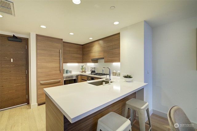 kitchen featuring sink, oven, a kitchen breakfast bar, light hardwood / wood-style floors, and kitchen peninsula