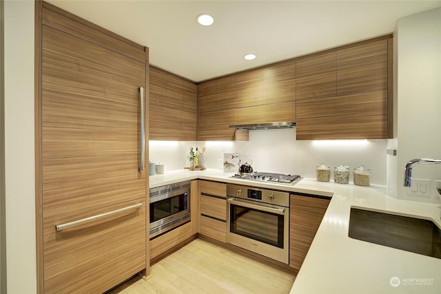 kitchen with exhaust hood, sink, built in appliances, and light hardwood / wood-style floors