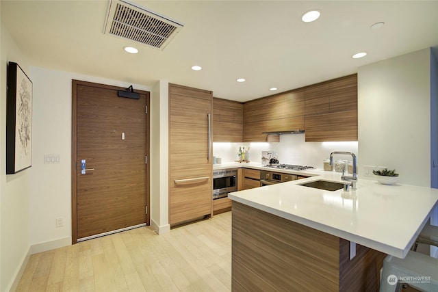 kitchen with sink, a kitchen breakfast bar, stainless steel gas cooktop, wall oven, and kitchen peninsula