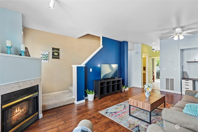 living room with a tiled fireplace, dark hardwood / wood-style floors, and ceiling fan