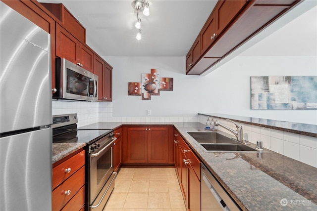 kitchen with tasteful backsplash, sink, dark stone counters, light tile patterned floors, and stainless steel appliances