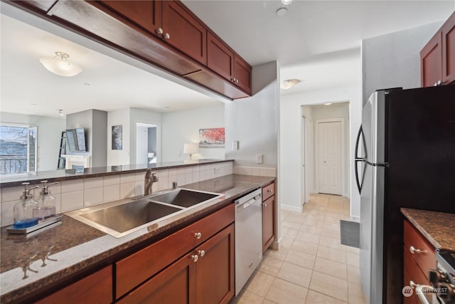 kitchen with appliances with stainless steel finishes, sink, decorative backsplash, dark stone counters, and light tile patterned floors