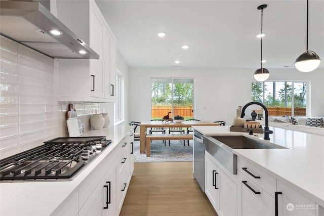 kitchen with wall chimney exhaust hood, stainless steel appliances, decorative light fixtures, and white cabinets