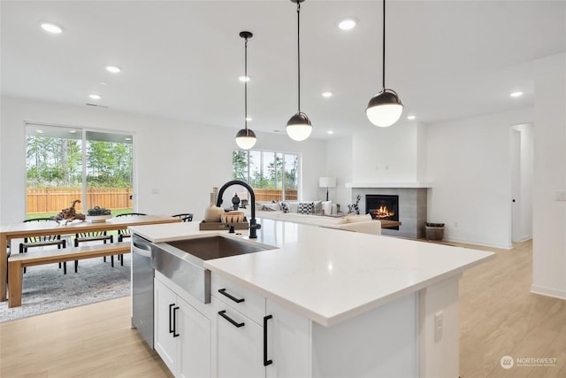 kitchen with a kitchen island with sink, pendant lighting, stainless steel dishwasher, and white cabinetry