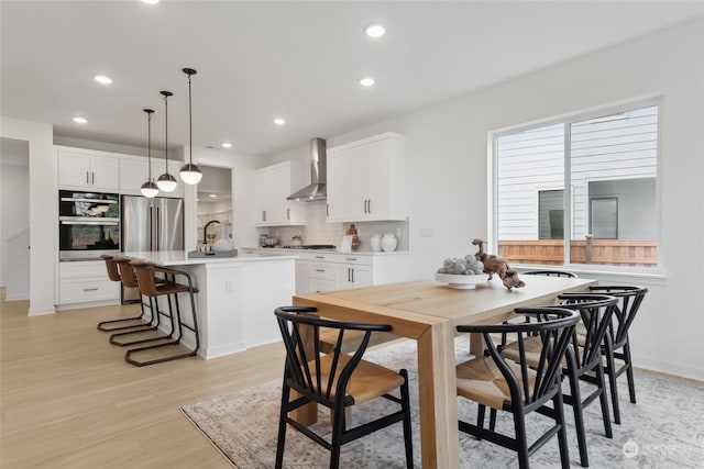 kitchen featuring white cabinetry, wall chimney exhaust hood, an island with sink, and hanging light fixtures