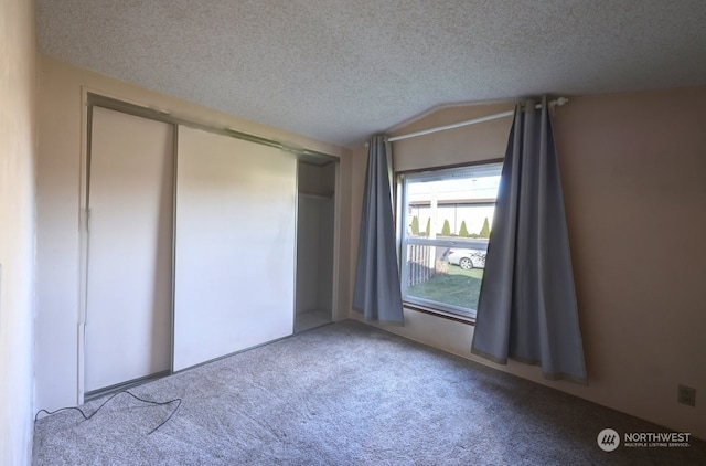 unfurnished bedroom featuring vaulted ceiling, a closet, a textured ceiling, and carpet