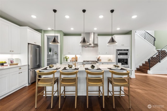 kitchen featuring stainless steel appliances, dark wood-type flooring, wall chimney range hood, and decorative light fixtures