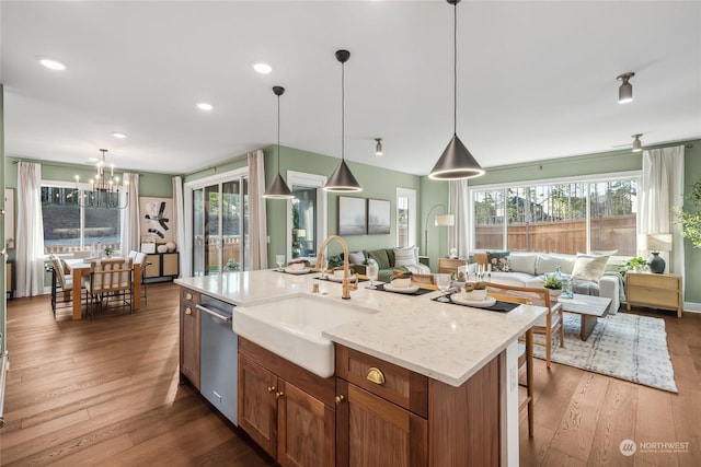 kitchen featuring pendant lighting, sink, a kitchen island with sink, stainless steel dishwasher, and light stone counters