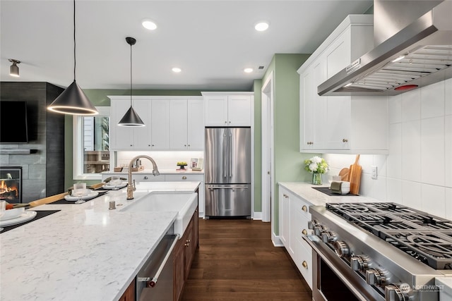 kitchen with hanging light fixtures, appliances with stainless steel finishes, light stone countertops, range hood, and white cabinets