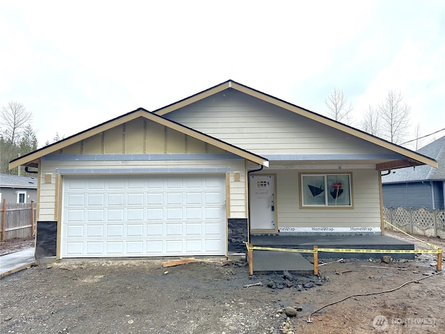 view of front facade with dirt driveway, board and batten siding, a garage, and fence