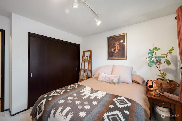 bedroom featuring rail lighting, light colored carpet, and a closet