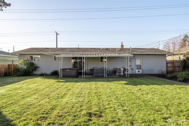 back of house with a hot tub, a patio, and a lawn