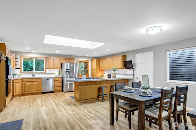 kitchen featuring sink, appliances with stainless steel finishes, a skylight, kitchen peninsula, and light wood-type flooring