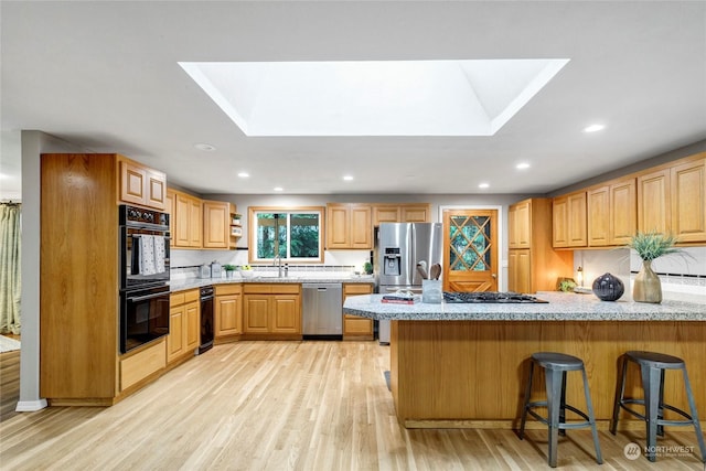 kitchen with light hardwood / wood-style flooring, a skylight, stainless steel appliances, a kitchen bar, and kitchen peninsula