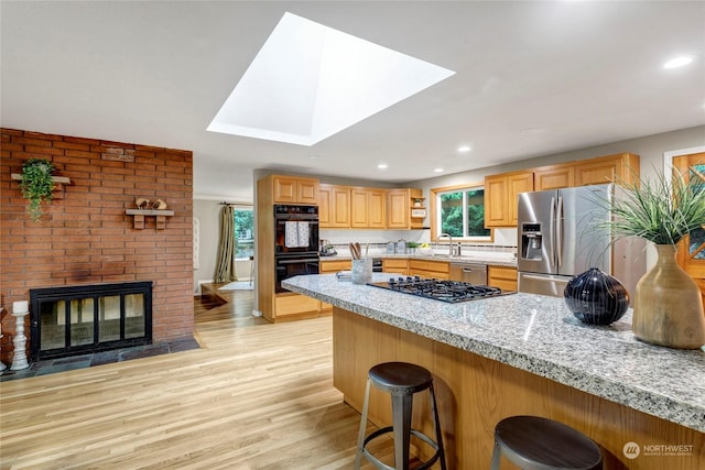 kitchen featuring a kitchen bar, sink, a brick fireplace, stainless steel appliances, and light hardwood / wood-style floors