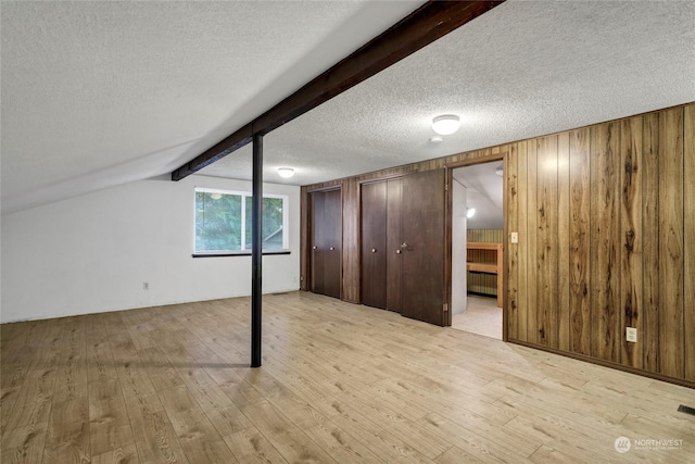 basement with light hardwood / wood-style floors, a textured ceiling, and wood walls