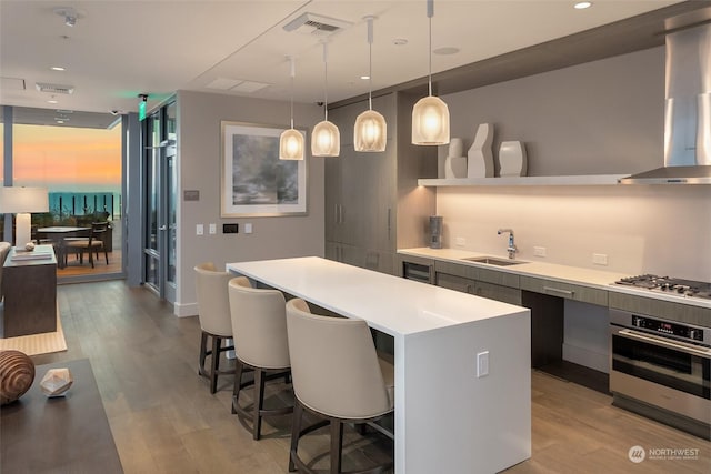 kitchen with decorative light fixtures, sink, a breakfast bar area, stainless steel appliances, and light hardwood / wood-style flooring