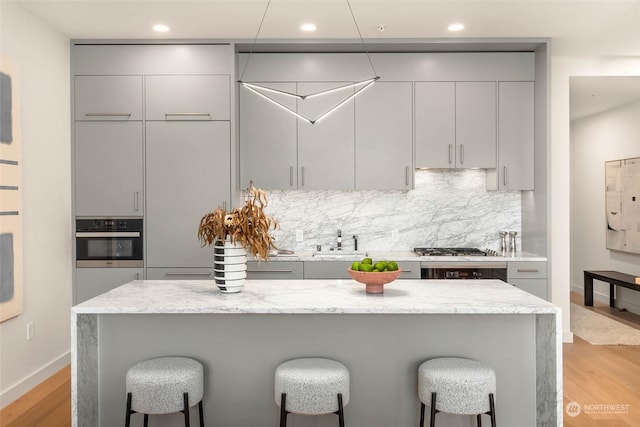 kitchen featuring gray cabinets, tasteful backsplash, light hardwood / wood-style floors, stainless steel appliances, and light stone countertops